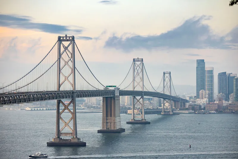Scenic view of the Bay Bridge and San Francisco skyline at dusk with a boat passing by.