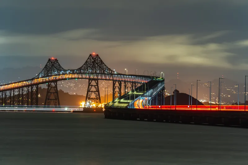 A stunning night view of an illuminated bridge with light trails against a city skyline.