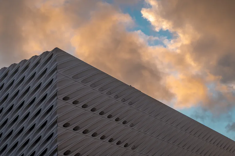A striking modern architectural facade with a dynamic sky backdrop at sunset.