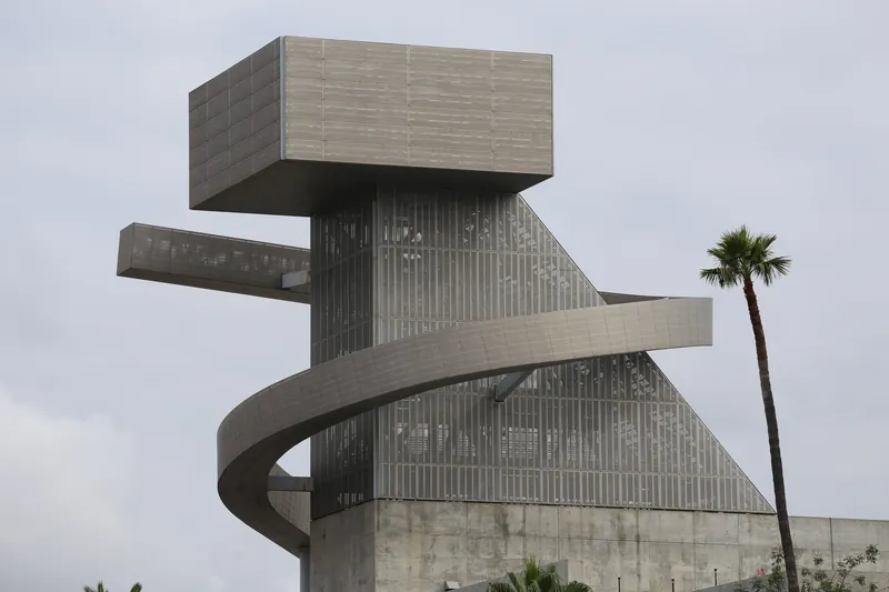 Modern architectural structure with a spiral design under cloudy skies and palm trees.