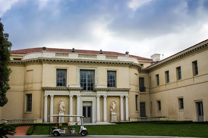 Elegant neoclassical building featuring grand columns, statues, and a golf cart on lush grass.