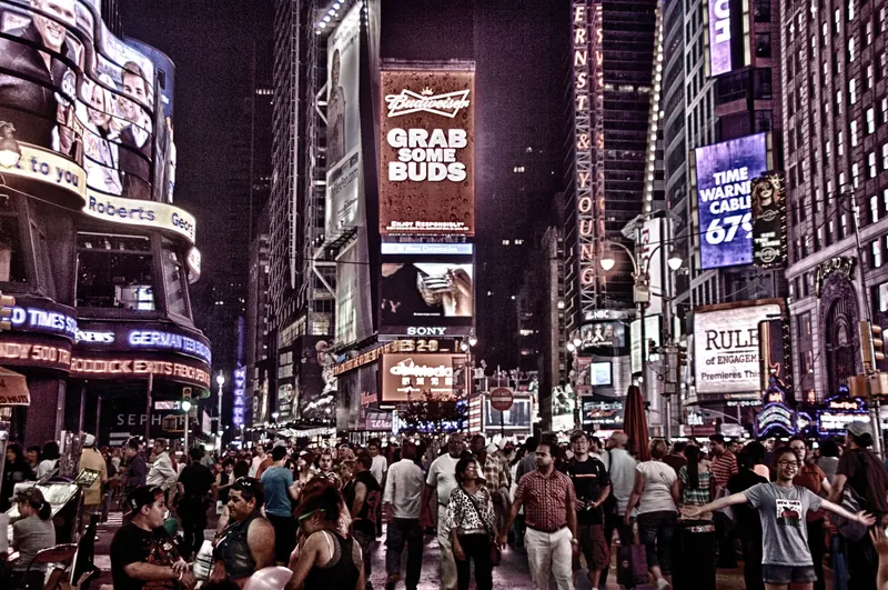 Bustling nighttime scene in Times Square, NYC, filled with colorful lights and diverse crowds.