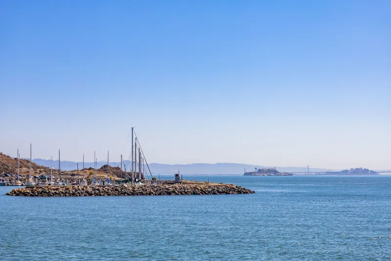 A tranquil view of San Francisco Bay with Alcatraz Island and sailboats under a clear blue sky.