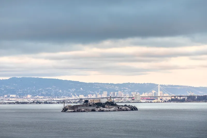 Skyline of San Francisco behind Alcatraz Island with overcast skies, showcasing iconic landmarks.