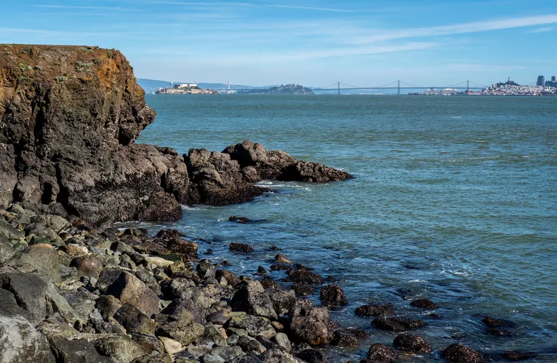 Rocky coastal scene with San Francisco Bay and Golden Gate Bridge in the distance.