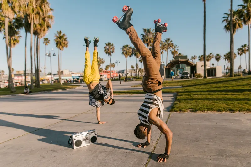 Two young men performing handstands on Venice Beach with a boombox nearby, showcasing fun and fitness.