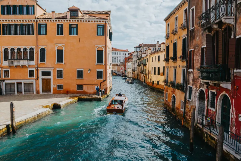 A picturesque scene of Venetian canal flanked by colorful historical buildings with a boat sailing through.