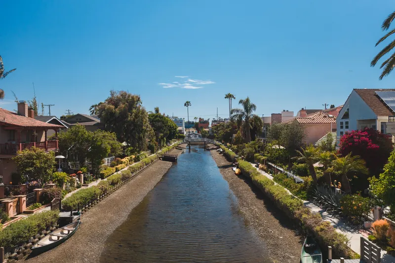 Sunny day view of Venice Canals in Los Angeles with lush gardens and classic architecture.
