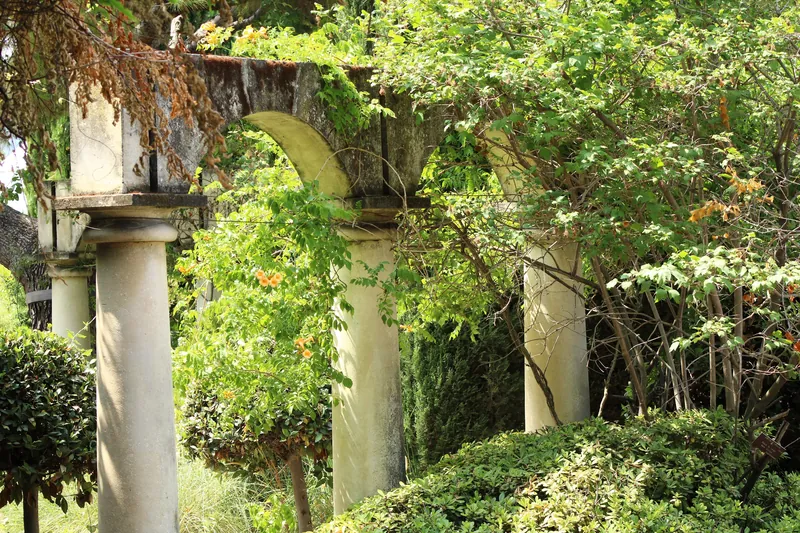 Serene garden scene featuring a stone archway surrounded by lush greenery and architectural pillars.