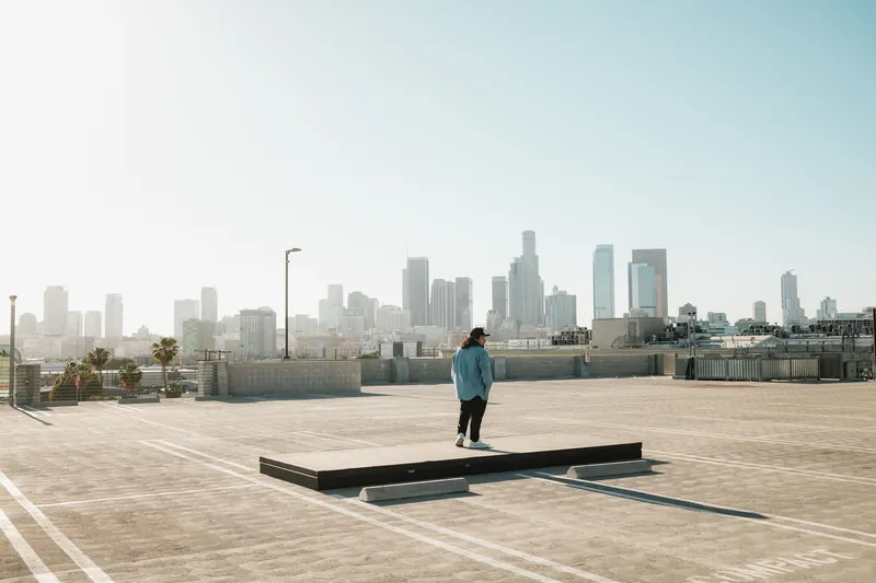 Individual on rooftop overlooking Los Angeles skyline, sunny day.