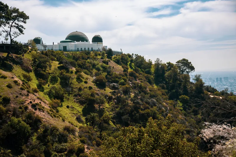 View of Griffith Observatory atop a lush hillside, overlooking Los Angeles cityscape.