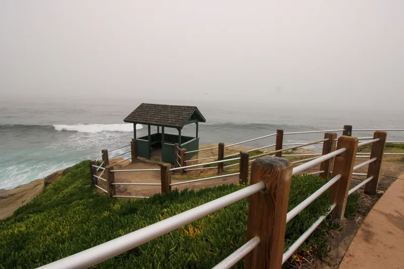 Misty morning view of a coastal lookout in La Jolla, San Diego, with green vegetation and ocean waves.